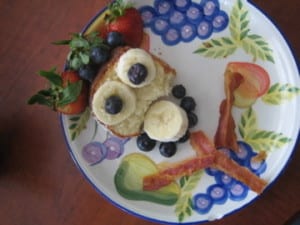 pound cake decorated like a person with bacon strips bananas blueberries and strawberries for a hat