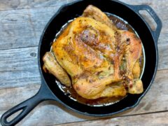Garlic Rosemary Lemon Chicken | Life At The Table. A whole roasted garlic, rosemary, and lemon chicken in a cast iron skillet sitting on a wooden table.
