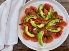 Grapefruit and Avocado Salad. Sliced grapefruit with sliced avocado arranged on a white plate garnished with lime juice, lime zest, salt, and a little drizzle of olive oil with a white napkin beside the plate.