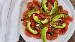 Grapefruit and Avocado Salad. Sliced grapefruit with sliced avocado arranged on a white plate garnished with lime juice, lime zest, salt, and a little drizzle of olive oil with a white napkin beside the plate.