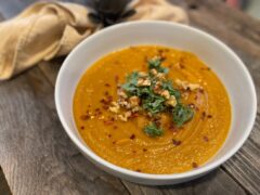Life At The Table Sweet Potato Soup. A white bowl filled with sweet potato soup garnished with kale, fresh ginger, walnuts and red pepper flakes.