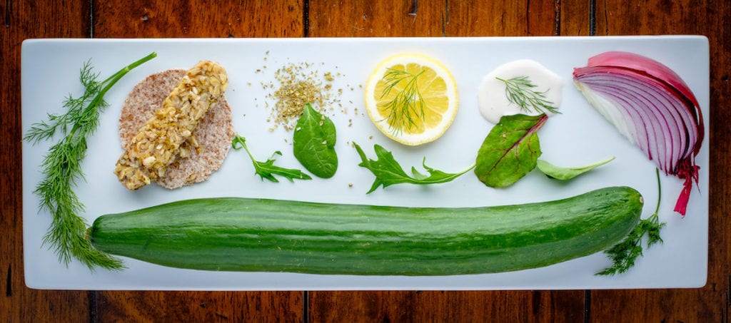 Greek Tempeh Wrap with Cashew Yogurt Tzatziki Sauce, garlic clove, cashew yogurt, dried oregano, dill, slice of lemon, onion, cucumber, on a long plate.