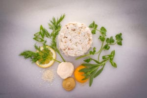 Crab cakes. Crab meat, green onions, dill, tarragon, cilantro, lemon zest, and a slice of lemon on top of a table.