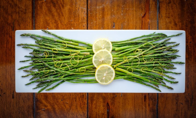 Roasted asparagus with lemon zest and slices of lemon at the center, on a plate.