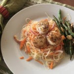 Life at the Table | Pan-Seared Scallops with Ginger and Garlic Rice Noodle Salad with baked string beans on the side, on a white plate atop a placemat with green table napkin