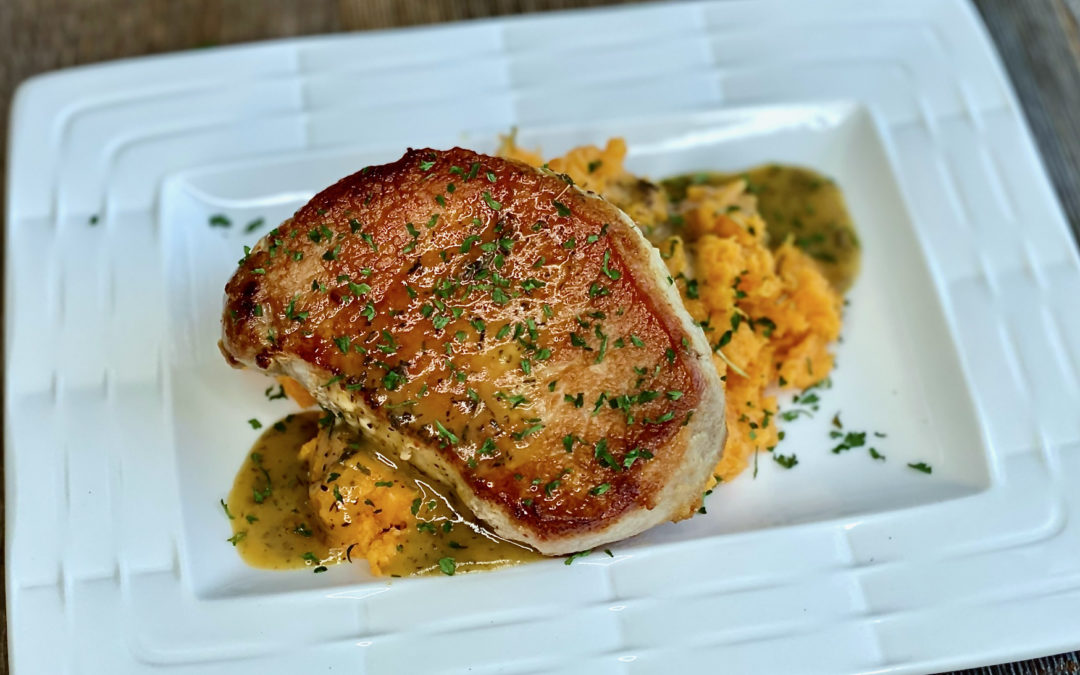 Life At The Table | Pan-Seared pork chops with a white wine, orange, thyme sauce served over mashed sweet potatoes on a white plate.