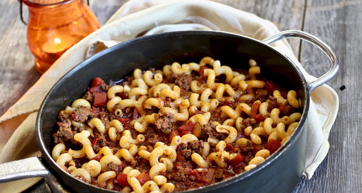Chili Mac on a pan with a table napkin beneath and a lamp on the side, on top of wooden table | Life at the Table