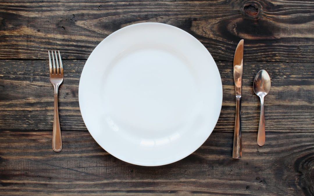 Life At The Table | Spending Time At The Table is Good Even for a Household of One single place setting on a wooden table with a fork to the left and knife and spoon to the right.