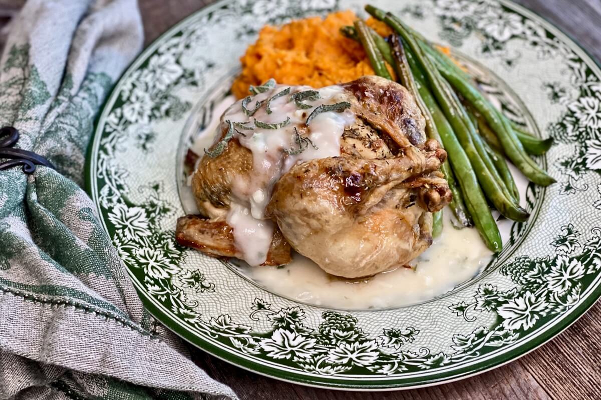 Life At The Table Virtual Cooking Experience Holiday Menu 2020 | Roasted Rock Cornish Game Hen, rosemary smashed sweet potato, sautéed green beans with lemon, and sage and garlic gravy artfully arranged on a holiday plate with a matching napkin lying beside it.