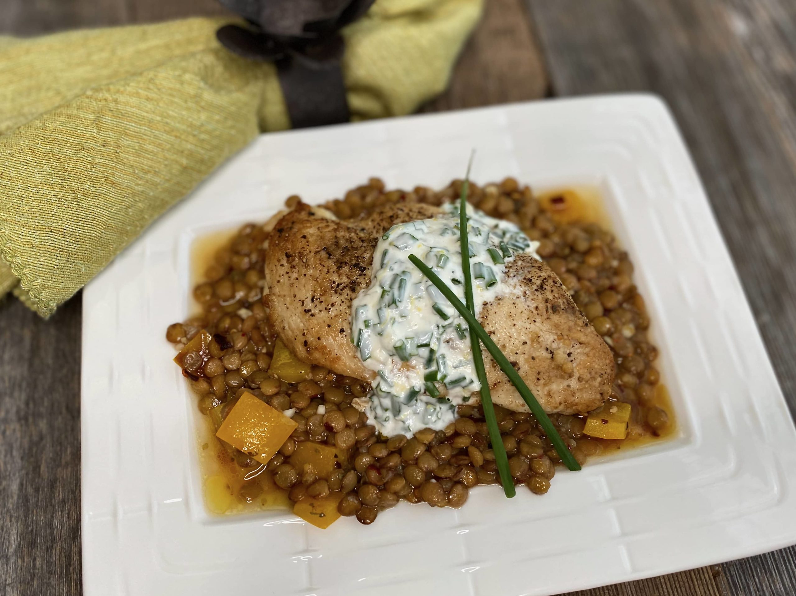 Life At The Table Lentils and Ladolemono Virtual Cooking Class | Pan-seared chicken with lentils and ladolemono on a white plate garnished with a chive and yogurt sauce.