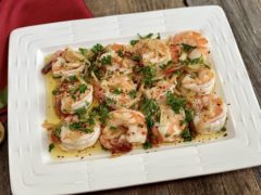 Life At The Table Shrimp al Ajillo. Shrimp al ajillo on a white plate garnished with parsley sitting on a wooden table with a red napkin beside it.