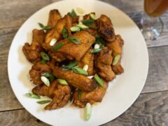 A pile of hot wings on a white plate garnished with green onion sitting on top of a wooden table.