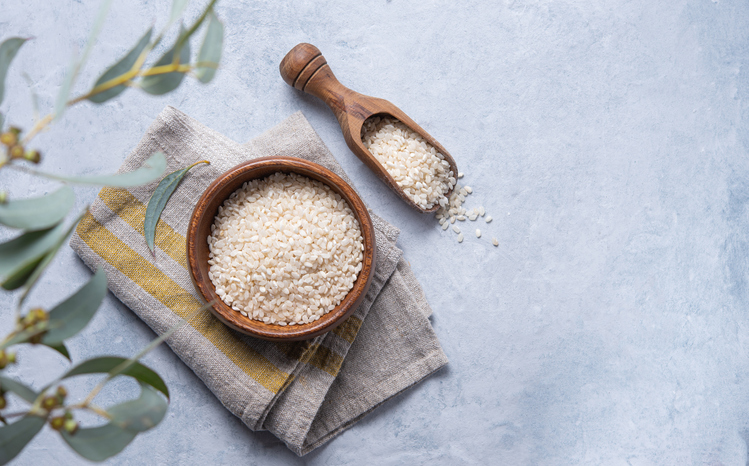 Arborio rice in a wooden bowl sitting on a napkin on a blue background