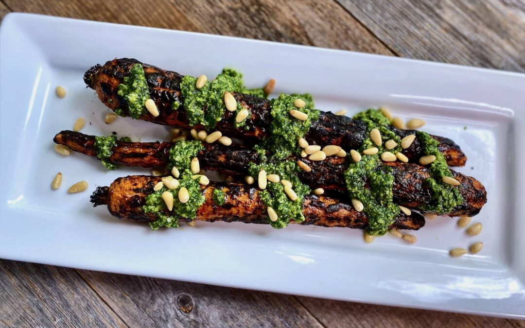 Life At The Table Grilled Carrots | three grilled carrots on a white platter garnished with basil pesto and pine nuts.