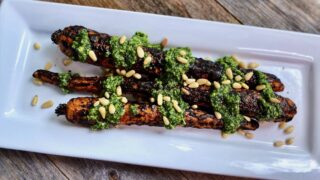 Life At The Table Grilled Carrots | three grilled carrots on a white platter garnished with basil pesto and pine nuts.