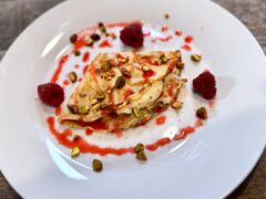 Life At The Table | Crepes with Mascarpone, Honey, and Orange. A crepe filled with mascarpone, honey, and orange on a white plate garnished with a raspberry coulis sauce and chopped pistachios.