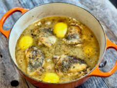 Herbs de Provence Chicken | Life At The Table. An orange dutch oven with herbs de Provence chicken with lemons sitting on a wooden table.