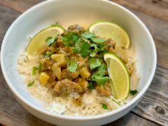 Life At The Table Fiji Chicken Curry. A bowl of Fiji Chicken Curry served on a bed of jasmine rice with fresh limes as a garnish in a white bowl sitting on a wooden table.