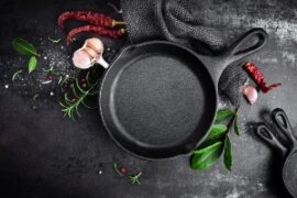 Life At The Table Health and Wellness Cooking Classes. Cast iron skillet on a dark tabletop surrounded by garlic, rosemary, and red chilis.