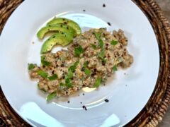 Life At The Table Poblano Sausage Gravy | A white plate with a biscuit that is covered with poblano sausage gravy and garnished with cilantro, red pepper flakes, and avocado on the side.