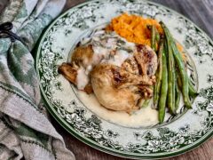 Life At The Table Roasted Cornish Game Hen on a green and white plate surrounded by green beans and mashed sweet potatoes. A napkin that matches the plate is lying beside the dish.