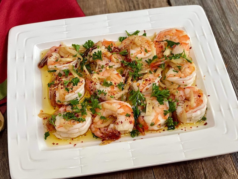 Life At The Table Shrimp al Ajillo Virtual Team Building Happy Hour. A white plate of shrimp al ajillo sitting on a wooden table.
