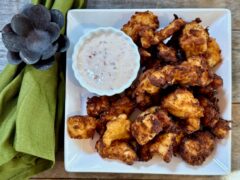 Homemade Chicken Nuggets | Life At The Table A white plate piled with chicken nuggets with a dipping sauce next to them on the plate and a green napkin lying on a wooden table next to the plate.