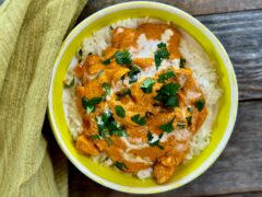 Life At The Table Butter Chicken. A bright green ceramic bowl filled with butter chicken, garnished with cilantro and a drizzle of cream.