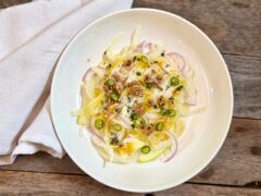 Shaved Fennel Salad. A shaved fennel salad with red onion, green apple, an orange vinaigrette, thai chili and candied sunflower seeds on a white plate with a white napkin beside it.