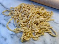 Life At The Table Homemade Pasta. Fresh pasta on a countertop with a rolling pin behind it.