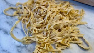 Life At The Table Homemade Pasta. Fresh pasta on a countertop with a rolling pin behind it.