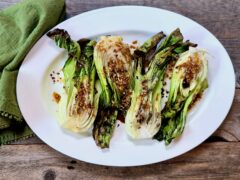 Life At The Table Grilled Baby Bok Choy. Grilled baby bok choy on a white platter garnished with a soy sauce and olive oil mixture with fresh garlic, fresh ginger, and red pepper flakes.