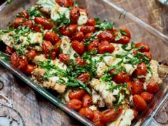 Life At The Table Caprese-Style Sheet Pan Chicken. A casserole dish Carprese-style chicken garnished with fresh basil and balsamic vinegar on a wooden table.